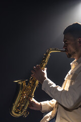 A European man plays the saxophone in the dark.