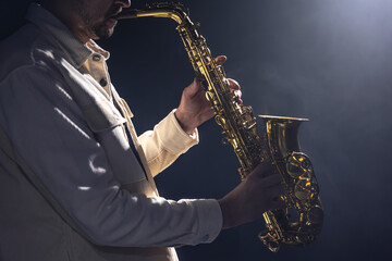 A European man plays the saxophone in the dark.