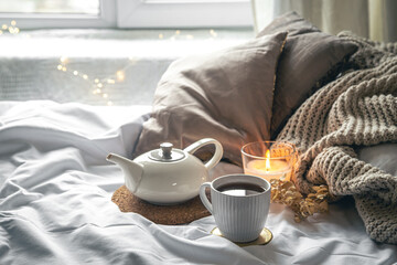 Cozy composition with a cup of tea, a teapot and a candle in the bed.