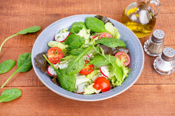 Green salad with fresh arugula, lettuce and tomatoes. Healthy vegan dish. Top view at wooden table. 