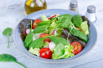 Green salad with fresh arugula, lettuce and tomatoes. Healthy vegan dish. Top view at wooden table. 
