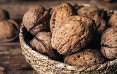 Close-up, whole walnuts in a wicker bowl on a wooden background.