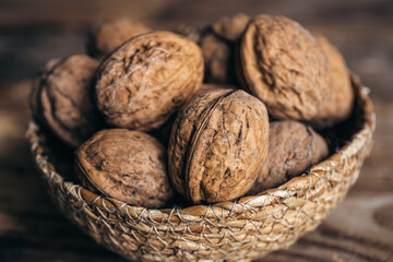 Close-up, whole walnuts in a wicker bowl on a wooden background.