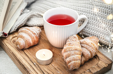 A cup of red tea, a candle, a croissant and a knitted element on a tray in bed.