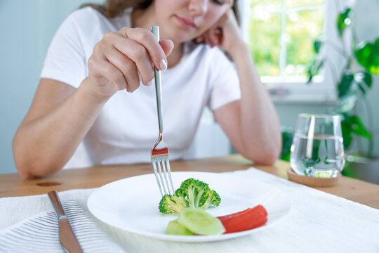 First day of diet. Unhappy young woman looking at small broccoli portion on the plate