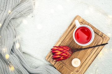 A cup of red tea and a flower on a wooden tray in bed, top view.