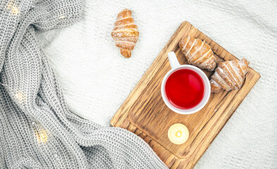 A cup of tea, a candle, a croissant and a knitted element in bed, top view.
