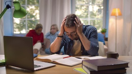 Young student at home desk reading tired a with pile of books and laptop. Realtime
