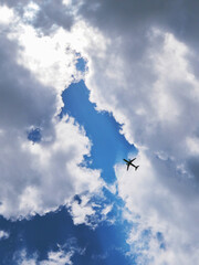 The passenger airplane is flying far away in the blue sky. Dramatic clouds with the sun shining through them. Aircraft in the air. Vertical illustration. Passenger air transportation