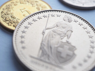 Swiss coins lie on light blue surface. 1 one frank coin close up. Illustration about economy, business or banking. Money and currency of Switzerland. Obverse of coin with figure of Helvetia. Macro