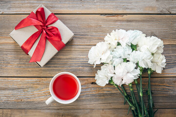 Bouquet of white flowers, gift box and a cup of tea on a wooden background.
