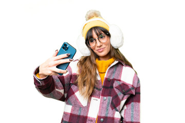 Young caucasian woman wearing winter muffs over isolated chroma key background making a selfie