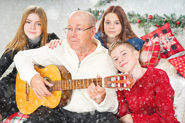 Grandfather playing guitar during christmas for grandchildren. Happy man 60s playing guitar christmas songs. Happy christmas atmosphere.