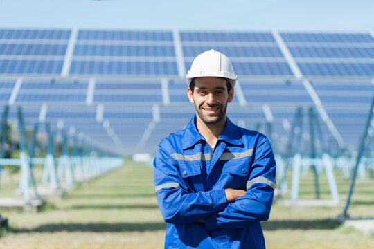 Portrait of smiling male engineers at the solor farm with solar panels blur background. Male electrician worker working by checking operation system at long rows of photovoltaic solar panels farm
