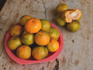 Oranges in a red dish on the wooden table