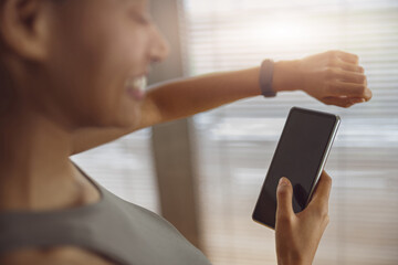 Smiling woman looking at sports watch and phone for checking her performance after exercise at home