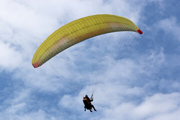 Yellow tandem Paraglider flying in a cloudy sky	