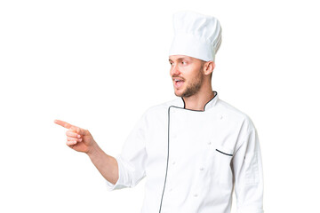 Young caucasian chef over isolated chroma key background pointing finger to the side and presenting...