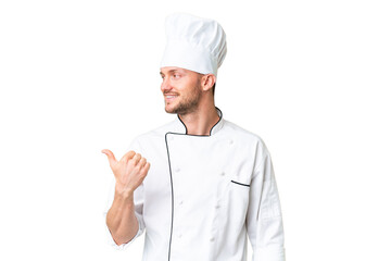 Young caucasian chef over isolated chroma key background pointing to the side to present a product