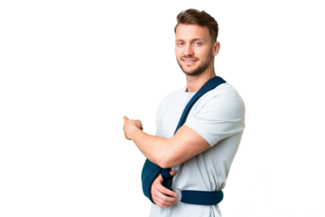 Young caucasian man with broken arm and wearing a sling over isolated chroma key background pointing back