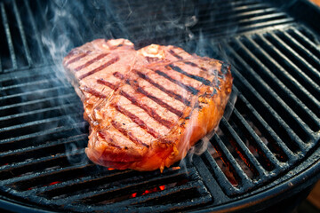Barbecue dry aged wagyu porterhouse beef steak grilled as close-up on a charcoal grill with fire and smoke