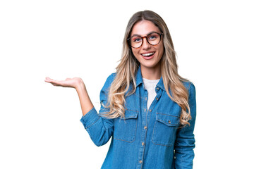 Young Uruguayan woman over isolated background holding copyspace imaginary on the palm to insert an...