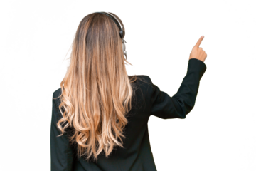 Telemarketer pretty Uruguayan woman working with a headset over isolated background pointing back with the index finger