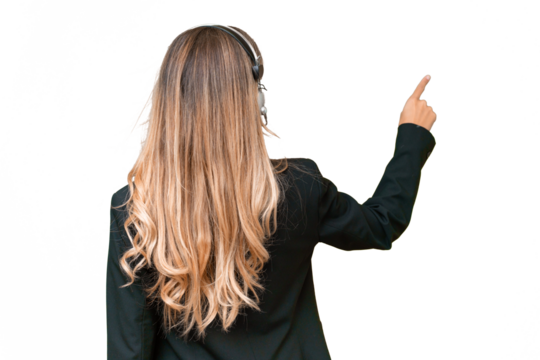 Telemarketer pretty Uruguayan woman working with a headset over isolated background pointing back with the index finger