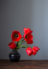 red tulips in dark ceramic vase on wooden table