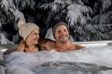 young couple relaxing in outdoor hot tub in winter