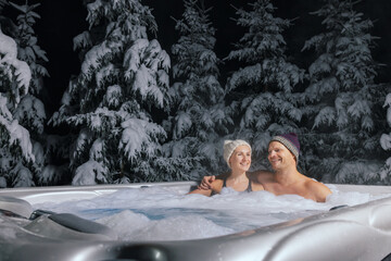 happy couple relaxing in outdoor jacuzzi at winter in resort spa hotel. romantic getaway - obrazy, fototapety, plakaty