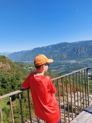 Fototapeta na wymiar young boy with cap standing on a bridge and looking over mountains