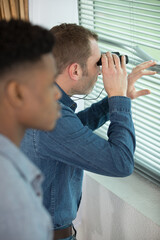 concerned men keeping watch through window with binoculars