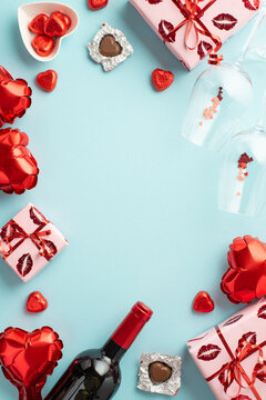 Top view vertical photo of gift boxes heart shaped balloons wine bottle glasses confetti and saucer with candies on isolated pastel blue background with empty space in the middle