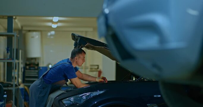 Auto mechanic repairs a car at a service station. Hood of the car is open.