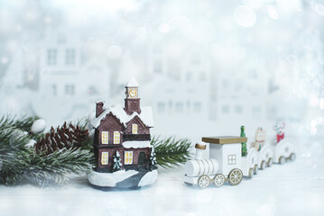Christmas card. Toy train, cabin, spruce tree line in front of the white city.