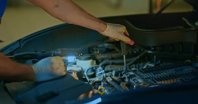 Male mechanic working on a car in a service station. Something is unscrewing on the car engine. Close-up