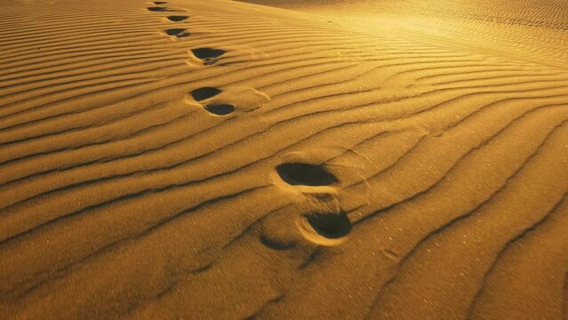 Camera follows footprints in big sand dune. Footprints in the sand in desert at warm sunset lights. UHD, 4K