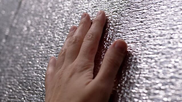 Female Hand touching the Rough Surface of a Heat Reflector Foil. Shiny, silver texture of thermal insulation material. Close-up. Light reflector. Heat protection. Texture, Background. Sunlight.