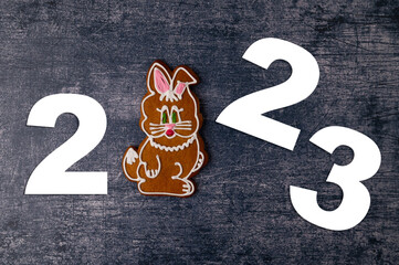 Year 2023 inscription with gingerbread in the shape of a rabbit with icing on the background of a dark blue metallic table. Year of the rabbit.