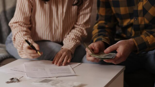 Signing agreement. Woman signs paper contract, and man counts money in cash. Hands close-up. Concept of buying real estate, leasing and insurance.