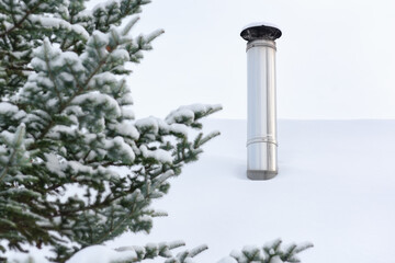 Iron chimney pipe. The roof is covered with a thick layer of snow. Large fir tree in front of a...