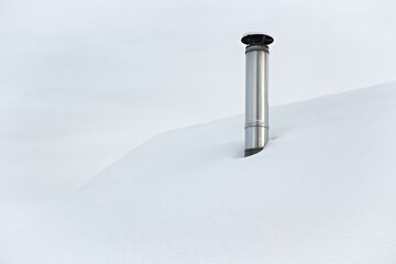 View of a tall metal chimney on a snow-covered roof. Snow covered roof.