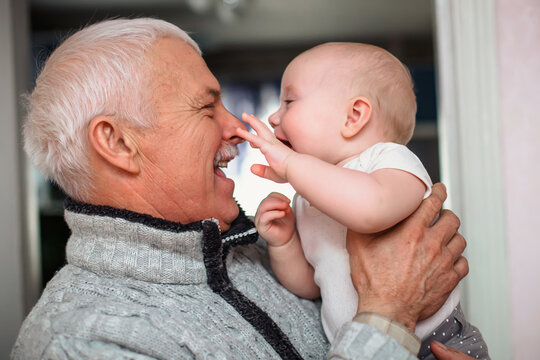 A newborn baby touches the old grandfather by the nose. An elderly man is having fun with his granddaughter. Happy generations. Family life