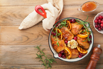 Baked chicken thighs with orange, cranberry and spicy herbs rosemary servered in frying pan on light wooden rustic background. Festive Christmas Dinner Concept menu. Top view. copy space