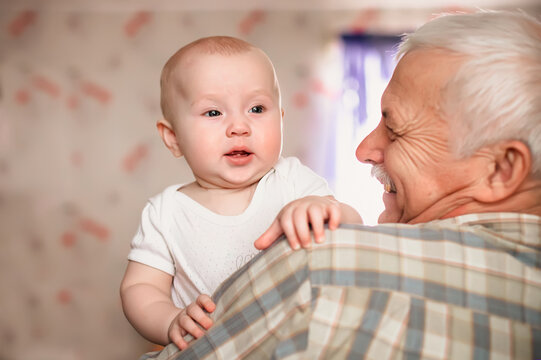 A 3-month-old baby smiles funny. Over shoulder close up of grandfather holding his baby grandson