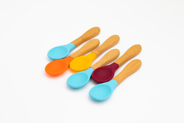 Six silicone spoons with bamboo handles of different colors on a white background. Cutlery is safe for babies