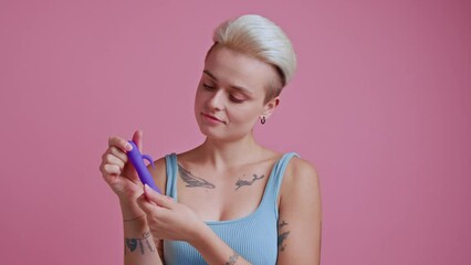 Sexy blonde woman looking playfully at the dildo toy over the pink background