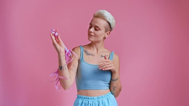 Excited woman playing with pink whip in hands and feeling playful over pink background