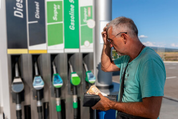 Mature man worrying and counting money, holding euro banknotes to pay high price of gasoline. Lack of money for gasoline and fuel. Expensive gasoline. Increase in gasoline prices concept. - obrazy, fototapety, plakaty